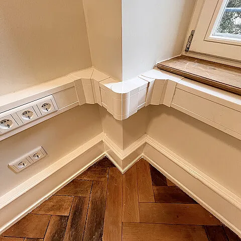 Detailaufnahme von Kabelkanal, Steckdosen und fertig verlegtem Holzboden im Innenausbau